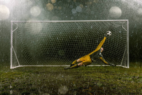 Dirty goalkeeper in flight catch the ball. Professional night rain stadium with football goal. Grass in the stadium wet from the rain