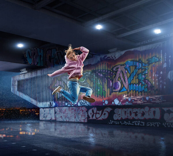 Female Hip Hop Dancer. Beautiful girl dancing at night on the background of graffiti wall