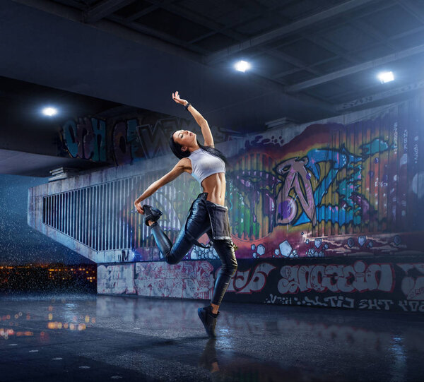 Female Hip Hop Dancer. Beautiful girl dancing at night on the background of graffiti wall