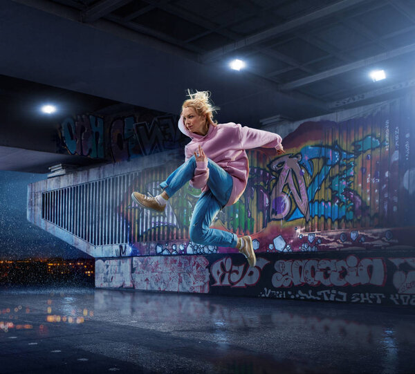 Female Hip Hop Dancer. Beautiful girl dancing at night on the background of graffiti wall