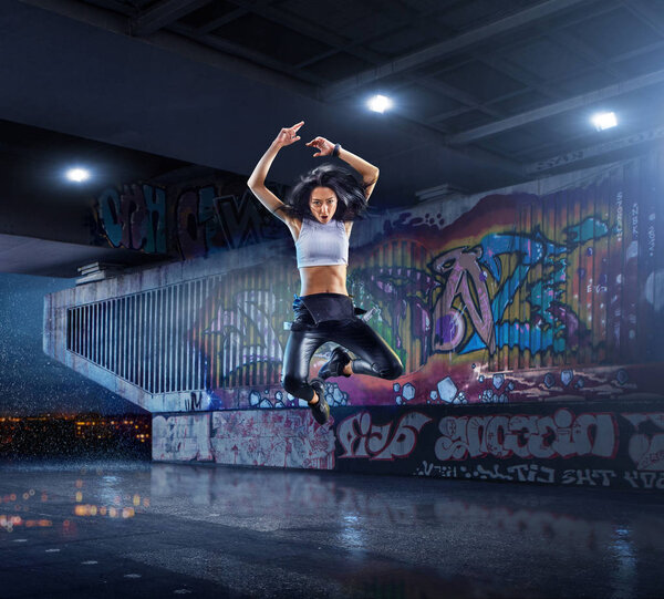 Female Hip Hop Dancer. Beautiful girl dancing at night on the background of graffiti wall