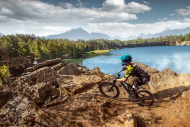 Orman yolunda dağ bisikletçisi. Erkek bisikletçi kayaya biniyor