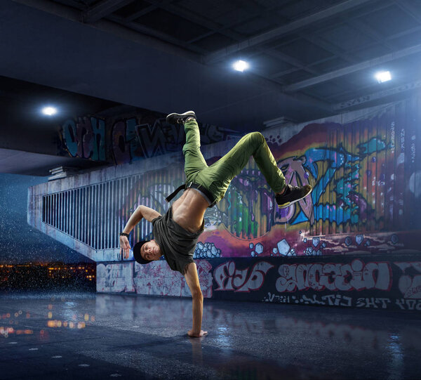 Male Hip Hop Dancer. Beautiful man dancing at night on the background of graffiti wall
