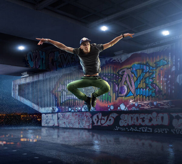 Male Hip Hop Dancer. Beautiful man dancing at night on the background of graffiti wall