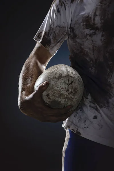 Rugby player hands with ball on dark background. Close up