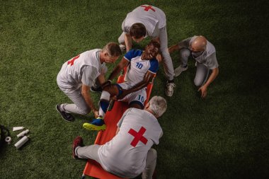 Futbol oyuncusu oyun sırasında bacak yaralandı. Spor doktorlar profesyonel bir futbol alanında oyuncuya ilk yardım sağlar