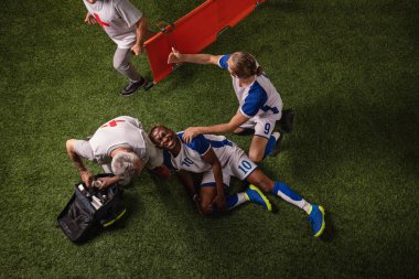 Soccer player injured leg during the game. Sport Doctors provide first aid to player on a professional football field clipart