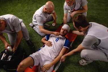 Futbol oyuncusu oyun sırasında baş yaralanması aldı. Spor doktorlar profesyonel bir futbol alanında oyuncuya ilk yardım sağlar