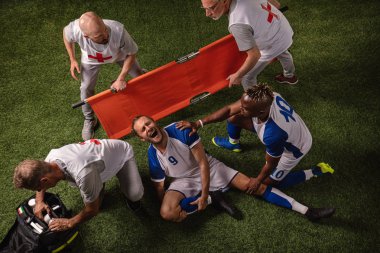 Futbol oyuncusu oyun sırasında bacak yaralandı. Spor doktorlar profesyonel bir futbol alanında oyuncuya ilk yardım sağlar