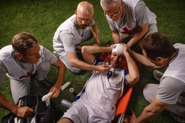 Futbol oyuncusu oyun sırasında baş yaralanması aldı. Spor doktorlar profesyonel bir futbol alanında oyuncuya ilk yardım sağlar