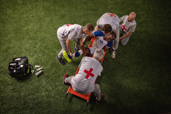 Soccer player injured leg during the game. Sport Doctors provide first aid to player on a professional football field
