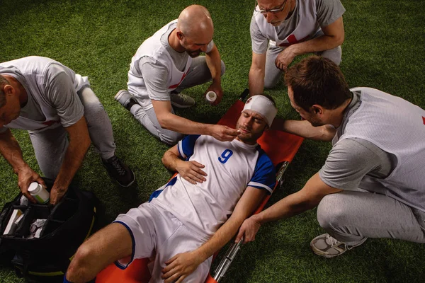 Soccer player received a head injury during the game. Sport Doctors provide first aid to player on a professional football field