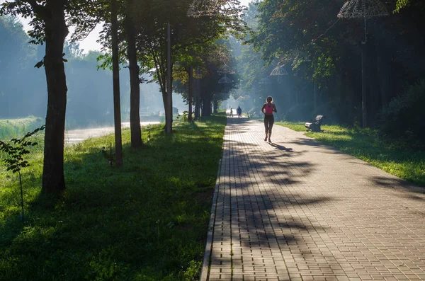 Morning jog in the park. The girl runs along the city street. Training at dawn. A woman walks on the pavement