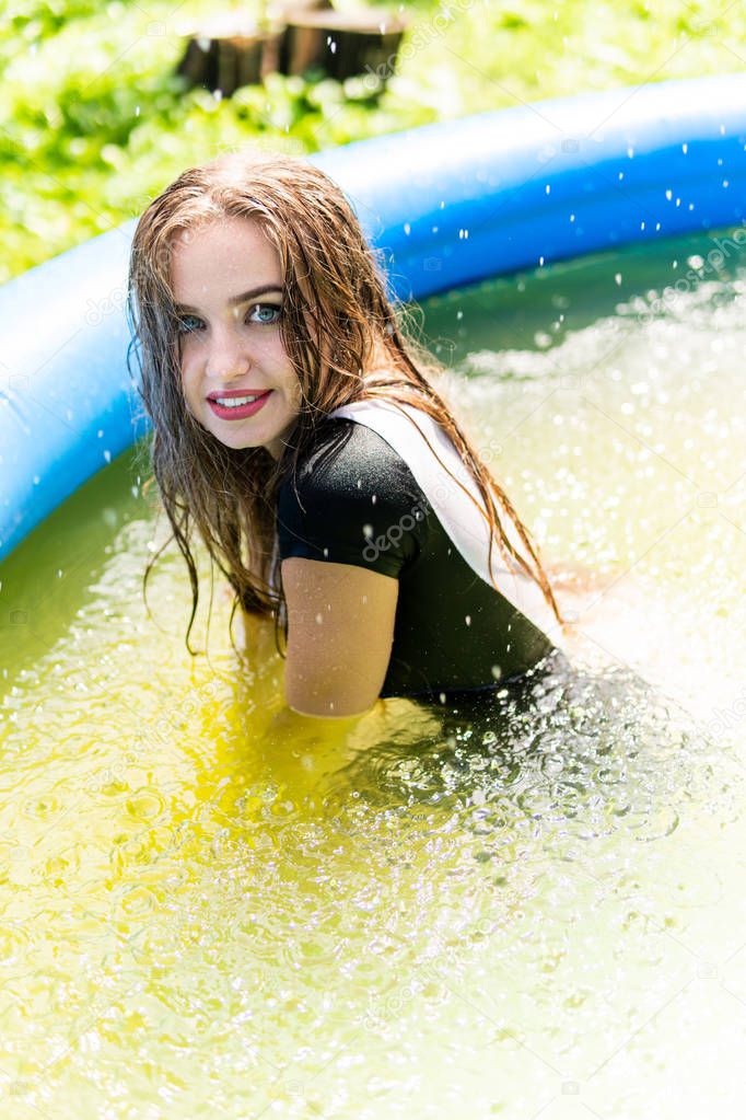 Beautiful female model dressed in long evening gowns, lies in the pool and sensually poses.