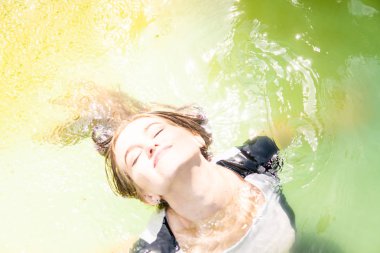 Güzel kadın model uzun akşam önlük giymiş, havuzda yatıyor ve sensually poz veriyor.