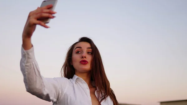 Retrato al aire libre de una hermosa chica tomando una selfie en el techo . —  Fotos de Stock