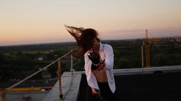 Молода дівчина в спортивній формі сидить на краю даху під час заходу сонця . — стокове фото