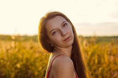 Haşhaş tarlasında poz veren gösterişli kırmızı elbiseli güzel bir kız. Gün batımında haşhaş tarlası. Sanat işleme. Günbatımı