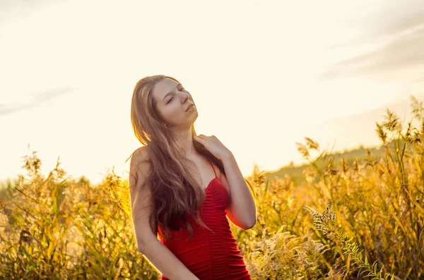 美丽的女孩，穿着时髦的红色连衣裙，在罂粟地上摆姿势。日落时分的罂粟田。艺术处理。日落 — 图库照片