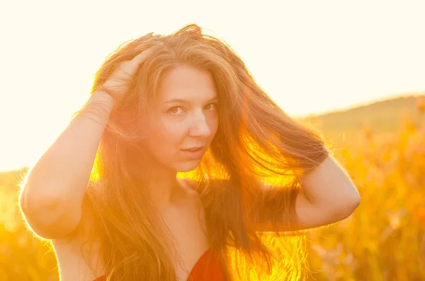 Belle fille dans une robe rouge chic posant sur un champ de pavot. Champ de pavot au coucher du soleil. Traitement de l'art. Coucher de soleil — Photo