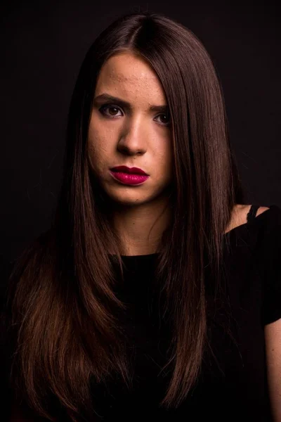 Portret van een mooie jonge vrouw in een zwarte jurk met een koele make-up en goede huid. Studio, zwarte achtergrond. — Stockfoto