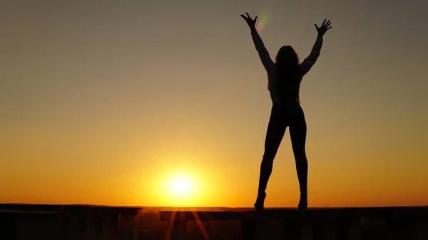 Jeune fille en uniforme de sport assis sur le bord du toit pendant le coucher du soleil . — Photo