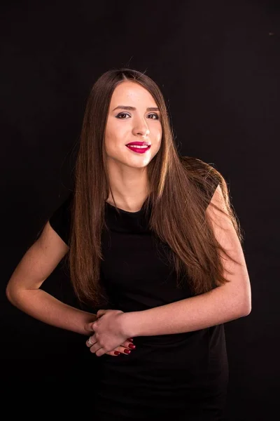 Retrato de una hermosa joven en un vestido negro con un maquillaje fresco y buena piel. Estudio, fondo negro . — Foto de Stock