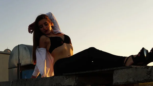 Menina jovem em uniforme esportivo senta-se na borda do telhado durante o pôr do sol . — Fotografia de Stock