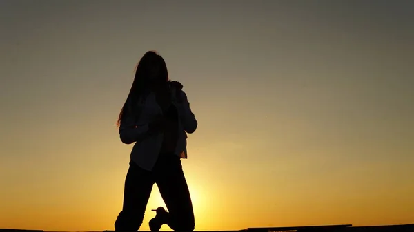 Young girl in sports uniform sits on the edge of the roof during sunset. — Stock Photo, Image