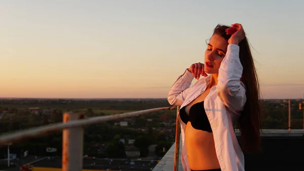 Menina jovem em uniforme esportivo senta-se na borda do telhado durante o pôr do sol . — Fotografia de Stock