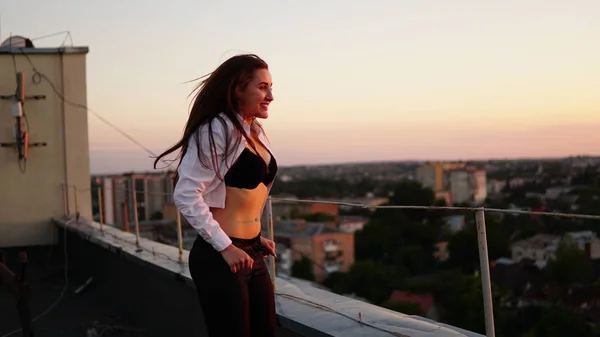 Молодая девушка в спортивной форме сидит на краю крыши во время заката . — стоковое фото