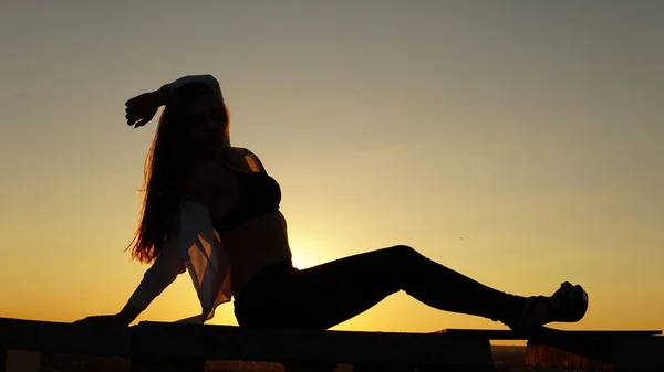 Nuori tyttö urheilu univormu istuu reunalla katon auringonlaskun aikana . — kuvapankkivalokuva