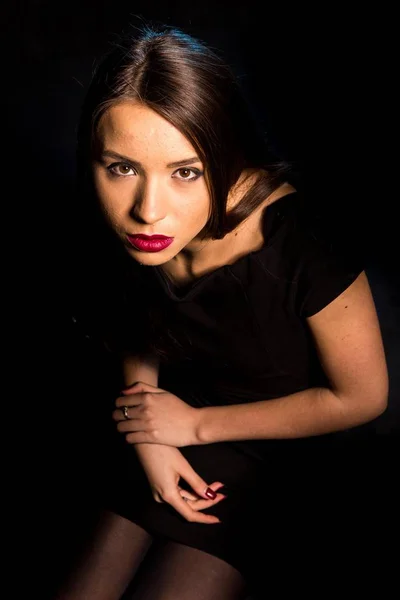 Porträtt av en vacker ung kvinna i en svart klänning med en cool makeup och bra hud. Studio, svart bakgrund. — Stockfoto