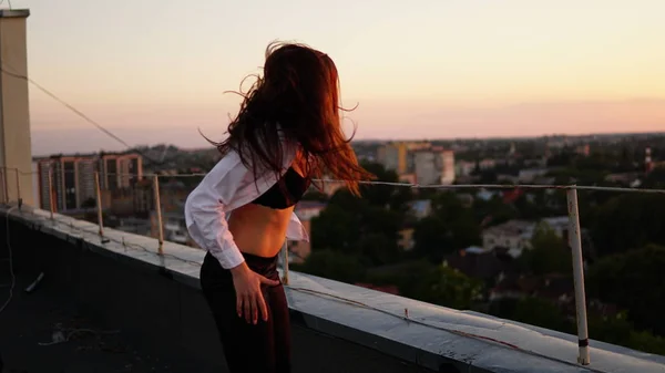 Jong meisje in de sport uniforme zit op de rand van het dak tijdens zonsondergang. — Stockfoto