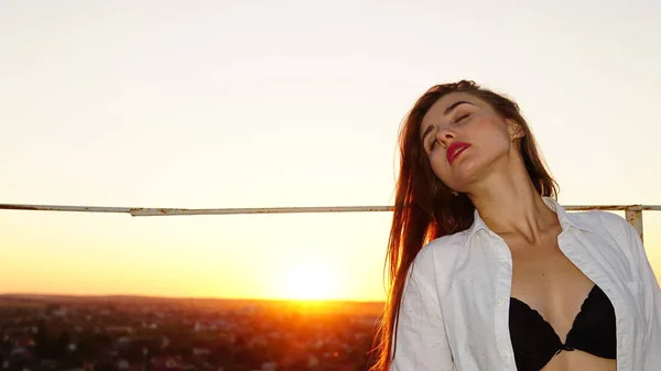 Young girl in sports uniform sits on the edge of the roof during sunset. — Stock Photo, Image