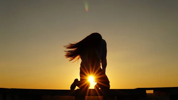 Молода дівчина в спортивній формі сидить на краю даху під час заходу сонця . — стокове фото