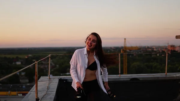 Jeune fille en uniforme de sport assis sur le bord du toit pendant le coucher du soleil . — Photo