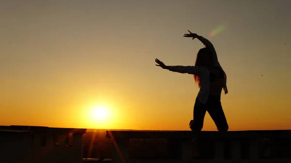 Jeune fille en uniforme de sport assis sur le bord du toit pendant le coucher du soleil . — Photo