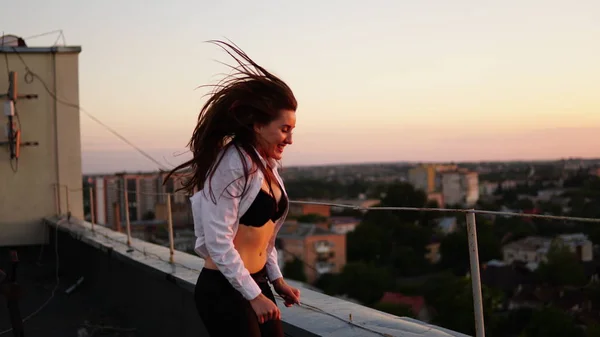Ung flicka i sport uniform sitter på kanten av taket under solnedgången. — Stockfoto