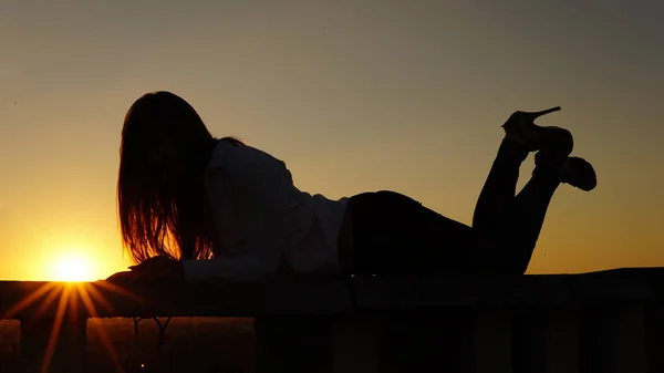 Jeune fille en uniforme de sport assis sur le bord du toit pendant le coucher du soleil . — Photo