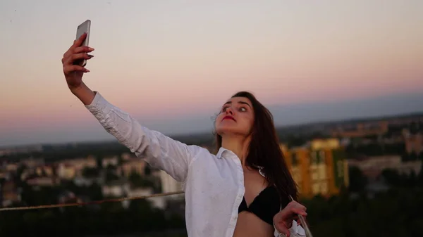 Retrato al aire libre de una hermosa chica tomando una selfie en el techo . — Foto de Stock