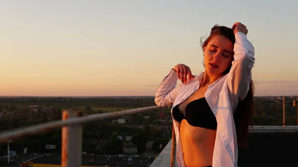 En ung jente i sportsuniform sitter på kanten av taket under solnedgang. . – stockfoto
