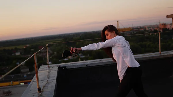 Young girl in sports uniform sits on the edge of the roof during sunset. — Stock Photo, Image