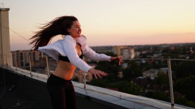 Genç kız spor Tekdüzen çatının kenarında günbatımı sırasında oturur..