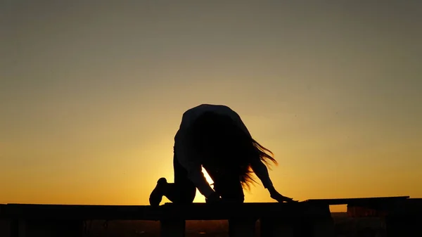 Young girl in sports uniform sits on the edge of the roof during sunset. — Stock Photo, Image