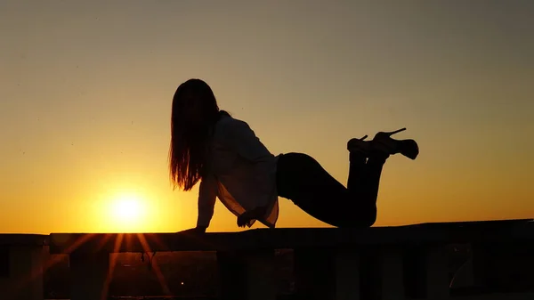 Jong meisje in de sport uniforme zit op de rand van het dak tijdens zonsondergang. — Stockfoto