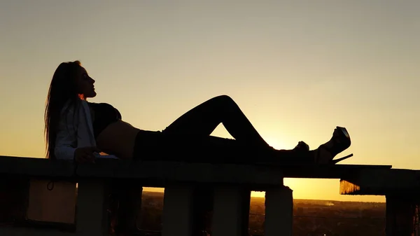 Chica joven en uniforme deportivo se sienta en el borde del techo durante el atardecer . —  Fotos de Stock