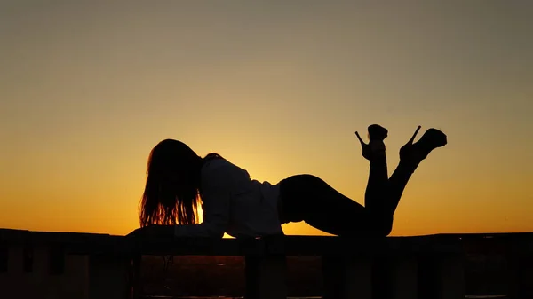 Menina jovem em uniforme esportivo senta-se na borda do telhado durante o pôr do sol . — Fotografia de Stock