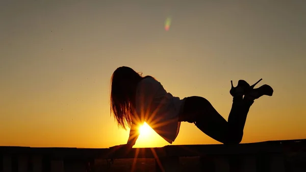 Sport egységes fiatal lány ül a tető szélén során naplemente. — Stock Fotó