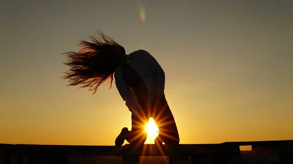 Junges Mädchen in Sportuniform sitzt bei Sonnenuntergang auf dem Dachrand. — Stockfoto